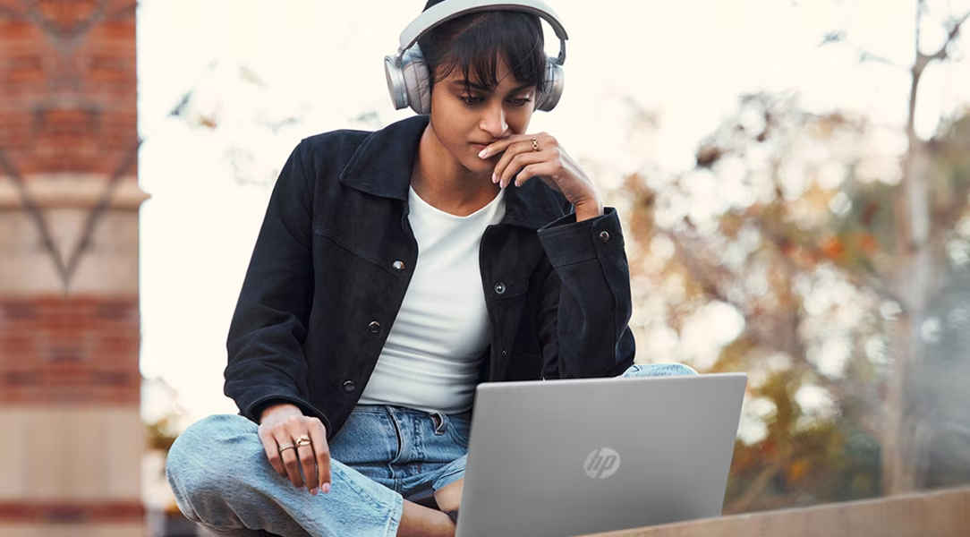 Chica con audifonos frente a su laptop HP