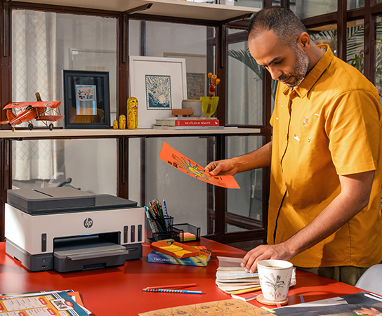 Imagen de un hombre con impresora HP Smart Tank sobre un mue...